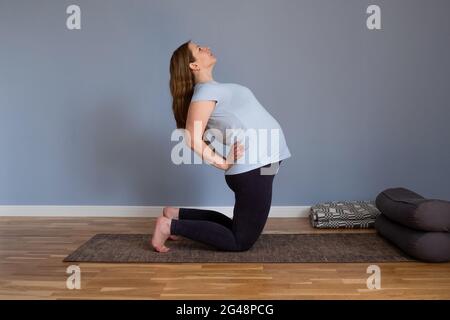 Donna in gravidanza sana di lunghezza intera che fa yoga che si esercita stretching a casa Foto Stock