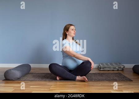 Donna incinta seduta sul pavimento in marichyasana stretching muscoli. Foto Stock