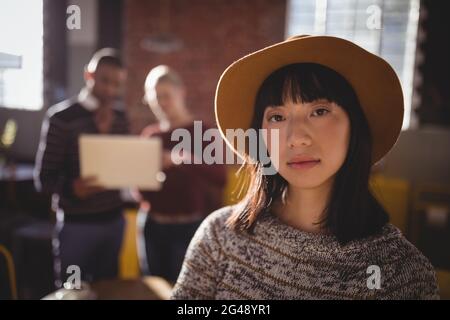 Ritratto di giovane donna sicura che indossa il cappello mentre si sta in piedi contro i colleghi Foto Stock