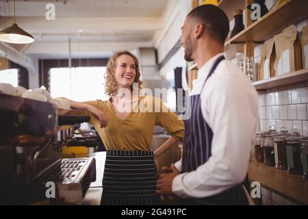Un giovane cameriere sorridente e una cameriera in piedi accanto alla macchina per caffè espresso Foto Stock