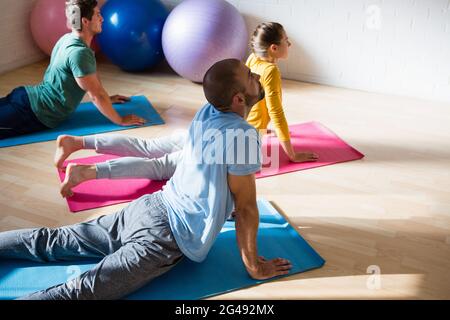 Vista ad alto angolo dell'istruttore di yoga con gli studenti che praticano la cobra in posa nel club Foto Stock