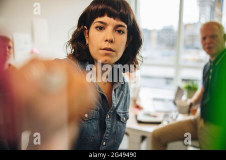 Brainstorming di giovane donna usando le note adesive sulla parete di vetro. Donna professionista che condivide le sue idee con i colleghi durante la riunione. Foto Stock