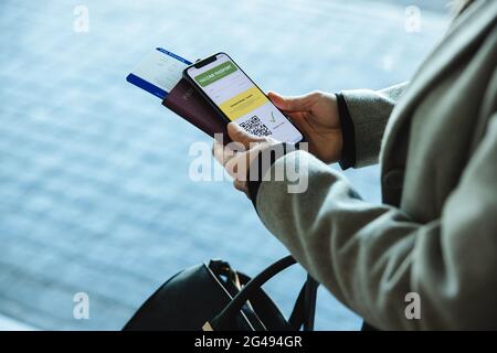 Vista a spalla di una donna in aeroporto con passaporto, biglietto e certificato di vaccinazione covid-19 sul suo cellulare. Donna che viaggia da ai Foto Stock