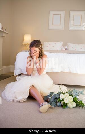 Sposa in abito da sposa piangendo mentre si siede a letto Foto Stock