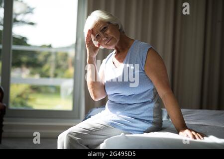 Donna anziana tesa seduta sul letto in camera da letto Foto Stock