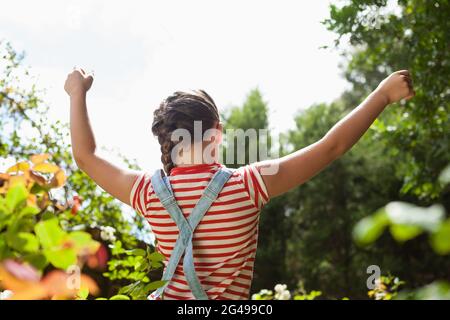 Vista posteriore della ragazza in piedi con le braccia sollevate tra le piante contro il cielo Foto Stock