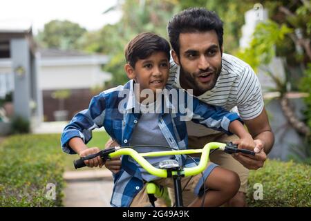 Padre che guarda via mentre assiste il figlio per andare in bicicletta Foto Stock