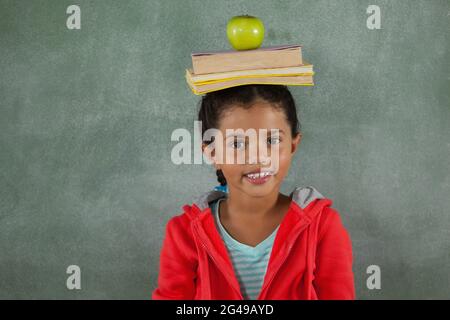 Giovane ragazza che bilancia libri e mela sulla testa Foto Stock