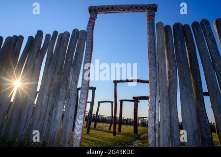 17 giugno 2021, Sassonia-Anhalt, Pömmelte: Il sole sorge sopra il santuario ad anello e si può vedere tra le lacune nelle stele di legno. Il fosso anulare è una ricostruzione di un sito culto che si dice esistesse lì dalla fine del periodo neolitico all'inizio dell'età del bronzo. Il 21 giugno 2021 si svolge il solstizio estivo. Poi inizia l'estate del calendario e i giorni diventano gradualmente di nuovo più brevi. Foto: Klaus-Dietmar Gabbert/dpa-Zentralbild/ZB Foto Stock