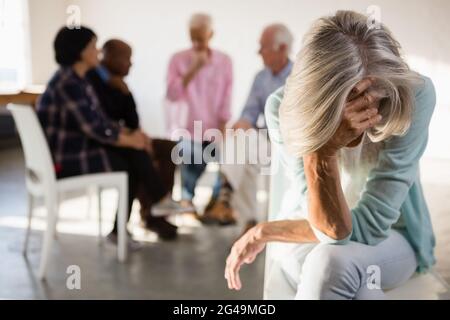 Donna anziana tesa con amici in background Foto Stock