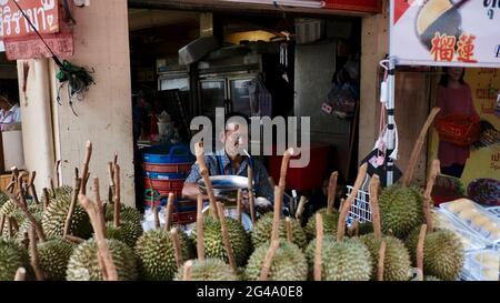 Cibo uomo che indossa camicia blu fumo sigaretta che vende frutta durian puzzolente è di fronte al suo negozio a Chinatown Bangkok Thailandia Foto Stock