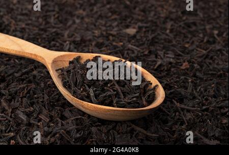 Foglie di tè secche in cucchiaio di legno isolato su sfondo scuro Foto Stock