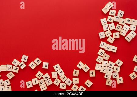 Immagine di sfondo le lettere sono sparse in disordine. Lettere inglesi. Lettere quadrate di legno su sfondo rosso brillante. Biglietto d'auguri, pronto all'uso Foto Stock