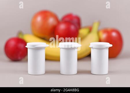 Piccole bottiglie con integratori alimentari di fronte a frutta e verdura su sfondo blu sfocato Foto Stock