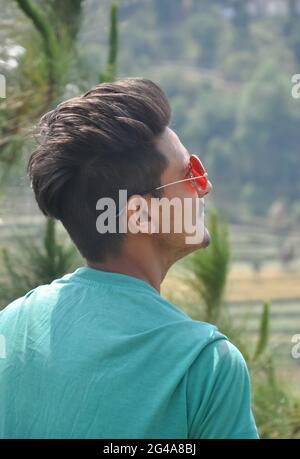 Vista da dietro di un bel ragazzo indiano giovane indossare occhiali da sole con lo sguardo in su mentre in piedi all'aperto nella natura Foto Stock
