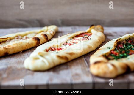 Un closeup di appetitosa varietà di pide flatbread ripieni di condimenti su una superficie di legno Foto Stock