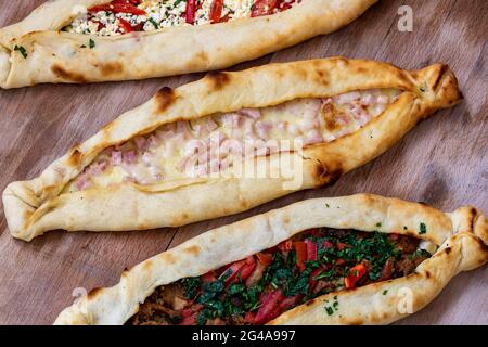 Una vista dall'alto di una appetitosa varietà di pani piatti di pide ripieni di condimenti su una superficie di legno Foto Stock