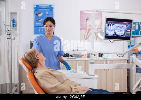 Assistente in clinica odontoiatrica che interroga pazienti anziani sui problemi dentali. Donna anziana che parla con l'infermiera medica in ufficio di stomatologia circa il problema dei denti. Foto Stock