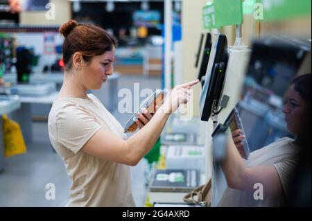 Una donna frustrato usa un contatore self-checkout. La ragazza non capisce come comprare indipendentemente generi alimentari nel supermercato senza un venditore Foto Stock