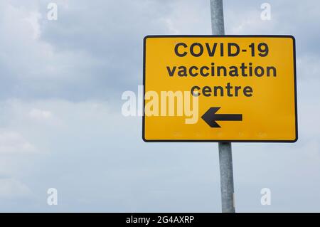 Indicazione gialla per un centro di vaccinazione COVID-19 con cielo nuvoloso sullo sfondo Foto Stock