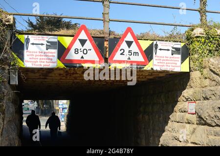 Cartelli di distanza sociale su un basso ponte ferroviario su uno stretto tunnel condiviso da pedoni e veicoli a motore. Foto Stock