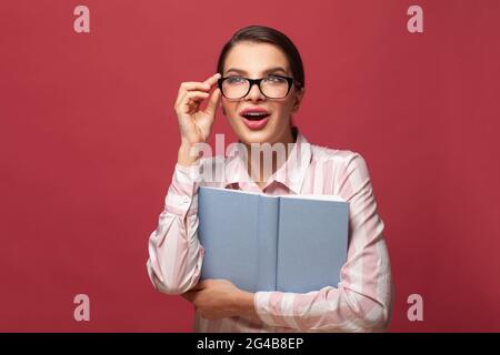 Ritratto giovane felice sorpresa donna in occhiali tiene libro. Lettura, educazione, studio e apprendimento del concetto di conoscenza. Studente sorridente, emo positivo Foto Stock