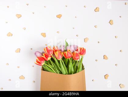 Primavera bellissimi fiori di tulipano in busta di carta artigianale su sfondo bianco con piccoli cuori di legno. Giorno della mamma, biglietto di auguri festivo decorativo fl Foto Stock