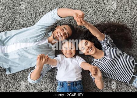 Vista dall'alto della famiglia allegra adagiato su un tappeto, tenendo le mani Foto Stock