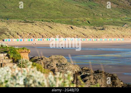 Capanne bianche, con porte colorate, si trovano di fronte alle dune con riflessi nella sabbia bagnata della spiaggia di Woolacombe Beach, Devon Foto Stock