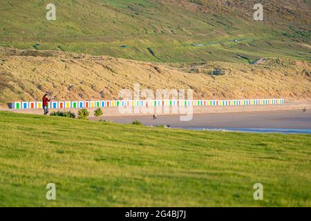 Capanne bianche, con porte colorate, si trovano di fronte alle dune con riflessi nella sabbia bagnata della spiaggia di Woolacombe Beach, Devon Foto Stock