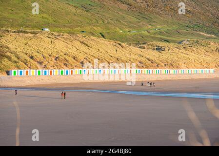 Capanne bianche, con porte colorate, si trovano di fronte alle dune con riflessi nella sabbia bagnata della spiaggia di Woolacombe Beach, Devon Foto Stock