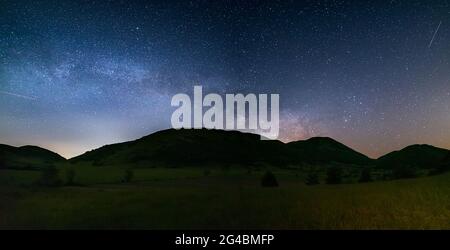 Cielo notturno panoramico sugli altipiani di Montelago, Marche, Italia. L'arco galassico della Via Lattea e le stelle che si innalzano da un paesaggio unico di colline verdi. Foto Stock