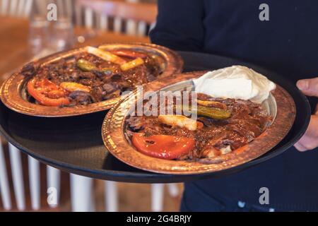 Cameriere che tiene piatti Iskender Kebab con cibo che serve gli ospiti in un ristorante. Foto Stock