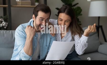 Emozionale felice giovane coppia di famiglia celebrare il successo, la lettura di notizie. Foto Stock