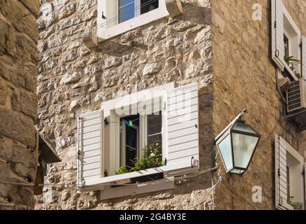 Un frammento della casa in pietra con finestra in legno con persiane bianche aperte e una lanterna all'angolo dell'edificio nel centro storico. Budva, Montenegro. Foto Stock