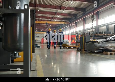 Team di operai in fabbrica che attraversano l'officina dell'impianto di compressione e discutono delle nuove attrezzature Foto Stock