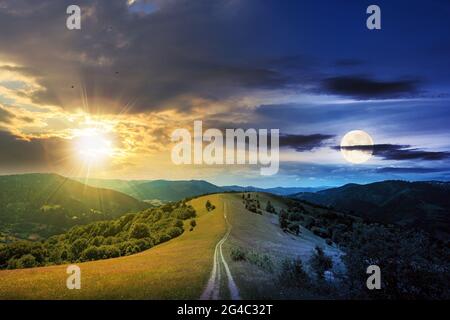 day and night time change concept above road through meadow in mountains. beautiful rural landscape of carpathians with sun and moon. wonderful summer Foto Stock