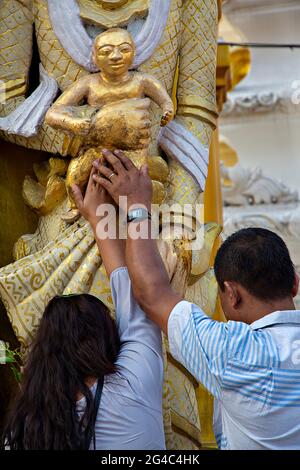 Coppia che prega il Buddha per desiderare avere un bambino nella pagoda di Shwedagon in Yangon, Myanmar Foto Stock