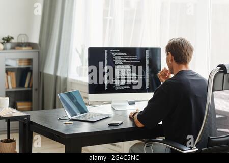 Vista posteriore del programmatore di computer seduto al tavolo di fronte al monitor di computer e lo sviluppo di software in ufficio Foto Stock