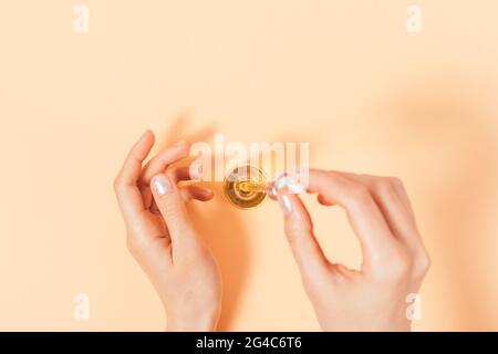 Primo piano le mani femminili gocciolano olio essenziale sulla pelle, sfondo beige, vista dall'alto. Foto Stock