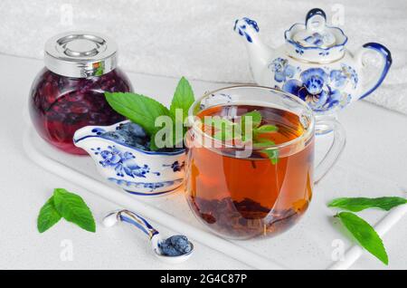 Una tazza di tè alla menta, frutti di miele freschi con marmellata sul piano di cucina. Festa del tè estivo Foto Stock