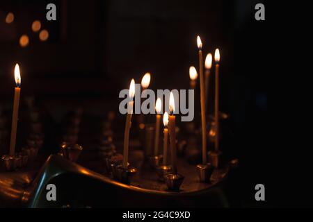 Piccole candele bruciano in una scura chiesa ortodossa, cristianesimo sfondo religioso Foto Stock
