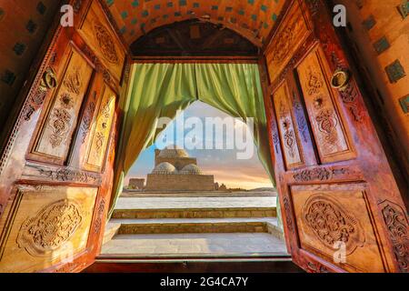 Vista sul mausoleo attraverso porte in legno al tramonto, nell'antico cimitero di Mizdakhan a Nukus, Uzbekistan Foto Stock