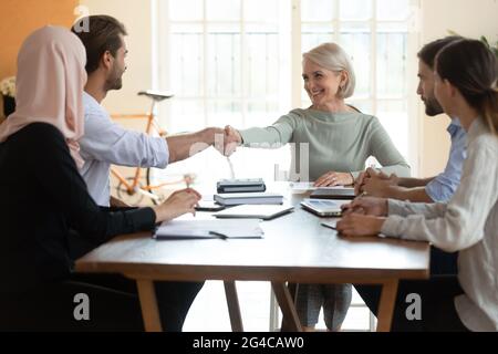 Sorridente dirigente di mezza età che scuote la mano di un uomo d'affari alla riunione aziendale Foto Stock