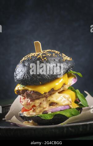 Doppio hamburger di manzo paty con un panino nero su sfondo scuro Foto Stock