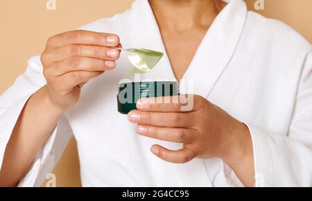 Immagine ritagliata delle mani femminili che tengono il vaso e che prendono il collagene sotto gli occhi macchie da esso, isolato su sfondo beige con spazio per il testo Foto Stock