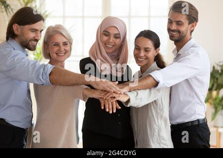 Felici e sorridenti dipendenti diversi che si riuniscono per le mani durante la riunione Foto Stock