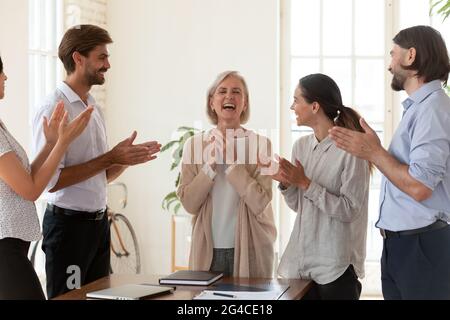 I dipendenti felici applaudono il dirigente di una donna d'affari di mezza età durante la riunione Foto Stock