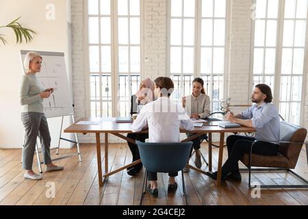 Team di dipendenti diversi che ascoltano una donna d'affari di mezza età durante la riunione Foto Stock