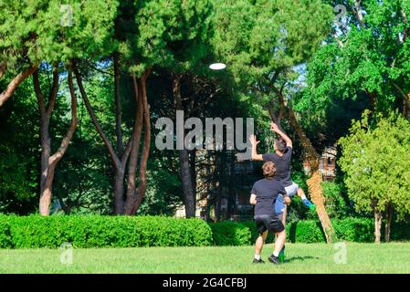 Gruppo di giovani adolescenti misti in abbigliamento casual che giocano con un disco volante di plastica in un parco oudoors. Uomo salto prendere un disco a un compagno di squadra Foto Stock